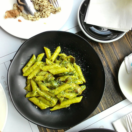 Penne pasta with pesto sauce in a black plate on a wooden tableの写真素材