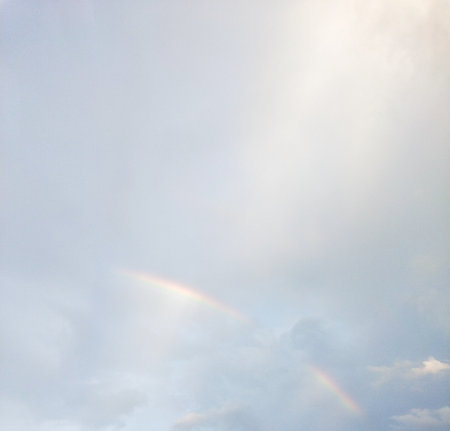 Rainbow in the blue sky with white clouds and sun beams.の写真素材