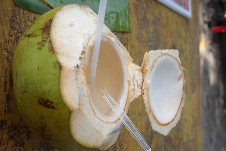 Freshly opened coconut with straws ready to drink. Coconut water is poured from the tap into the coconut. coconut milk with coconut on wooden tableの写真素材