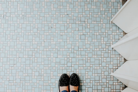 Top view of woman legs in black shoes and paper plane on blue tile floor.