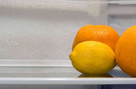 A lemon and two oranges inside fridge, sitting alone on the shelf. Copyspace provided.の写真素材