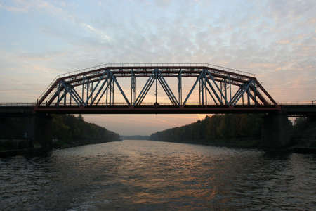 The iron railway bridge over the river in sunset.