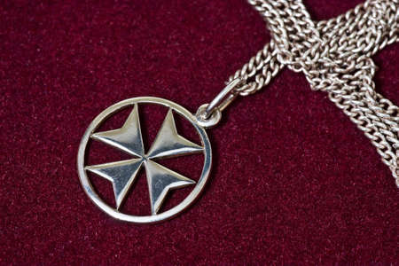 A Maltese cross silver pendant on velvet background.の写真素材