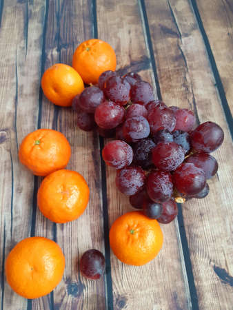 a wooden table top with loose fruit, mandarins and dark red grapesの写真素材