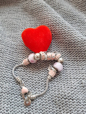 gray background, fabric, on it lies a small red heart and a braceletの写真素材