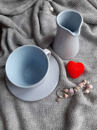 on a light silvery background a blue cup, a milk jug next to a small red heart and a braceletの写真素材