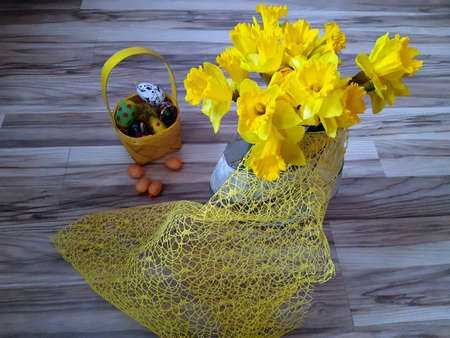 in the foreground yellow daffodils flowers and an Easter basket with eggs and easter eggs in the backの写真素材