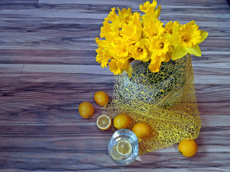 a large bunch of daffodils in a vase next to it is water with lemon and there are lemonsの写真素材