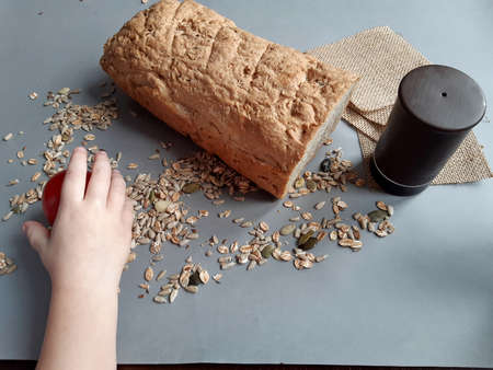 on the table you can see bread next to a stoneware salt shaker scattered pumpkin sunflower seeds a small children's hand reaches for a tomato lying next to it,の写真素材