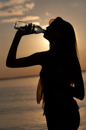 silhouette of girl drink water on water/sky background