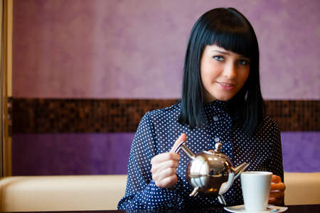 woman in cafe filling cup with teapotの写真素材