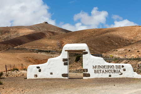 Typical municipality sign (white arch gate) near Betancuria village with desert mountain landscape in the background, Fuerteventura, Canary Islands, Spainのeditorial素材