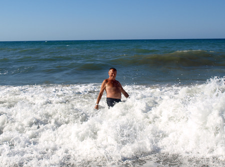 A senior man is standing in the sea-wave on the beach in Chania. Crete island, Greeceのeditorial素材