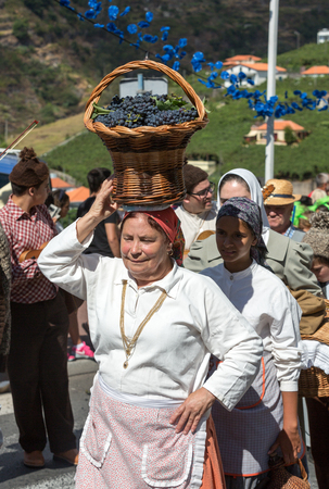 ESTREITO DE CAMARA DE LOBOS, PORTUGAL - SEPTEMBER 10, 2016: Woman wearing in traditional costume with a basket of grapes on her head at Madeira Wine Festival in Estreito de Camara de Lobos, Madeira, Portugal. The Madeira Wine Festival honors the grape harのeditorial素材