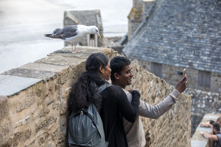 Le Mont-Saint-Michel, France - September 13, 2018: A pair of Hindus take a picture with a seagull in Mont Saint-Michel, the monastery and village on a tidal island between Brittany and Normandy, Franceのeditorial素材