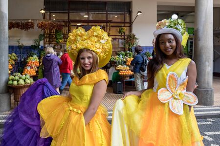 Funchal, Madeira, Portugal - April 23, 2018: Two beautiful girls in yellow dresses encourage shopping at Mercado dos Lavradores fruit and vegetable market in Funchal on Madeira Island. Portugalのeditorial素材