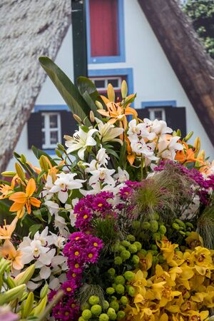 A floral composition with tropical flowers and a traditional house from Santana in the background. Madeira, Portugalの写真素材