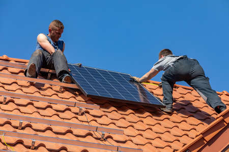 Ochojno, Poland - April 8, 2020: Workers installing solar electric panels on a house roof in ...