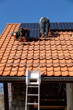 Ochojno, Poland - April 8, 2020: Workers installing solar electric panels on a house roof in...