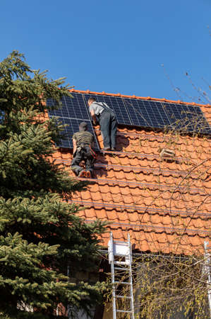 Workers installing solar electric panels on a house roof in Ochojno. poland