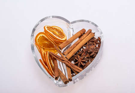 Slices of dried oranges, cinnamon and cardamom in a heart-shaped glass dish