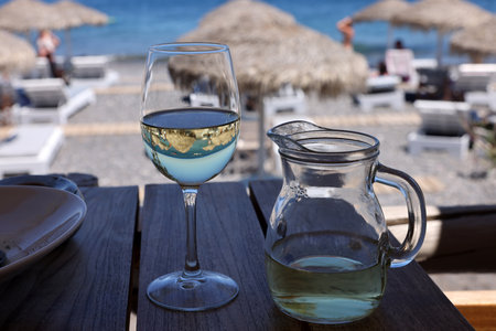 A glass of white wine at a restaurant by the beach in Kamari, Santorini. Greeceの写真素材
