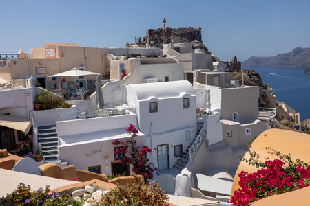 Oia, Santorini, Greece - July 3, 2021: Whitewashed buildings and the ruins of Castle of Agios Nikolaos on the edge of the caldera cliff, Oia village, Santorini, Greeceのeditorial素材