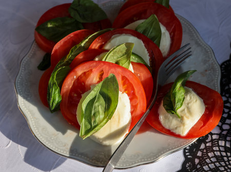 Tasty mozzarella cheese with basil and tomatoes on white plateの写真素材