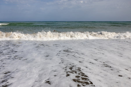 Foamy sea waves on the sandy beach of Bajondillo in Torremolinos, Malaga, Costa del Sol, Spainの写真素材