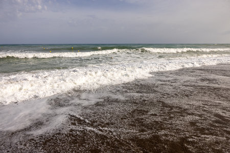Foamy sea waves on the sandy beach of Bajondillo in Torremolinos, Malaga, Costa del Sol, Spainの写真素材