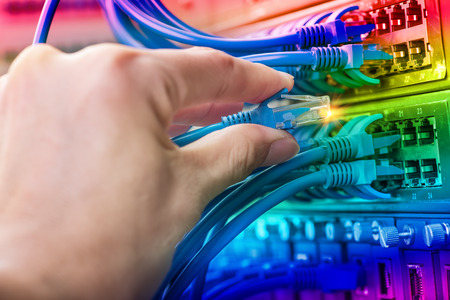 man working in network server room with fiber optic hub for digital communications and internet