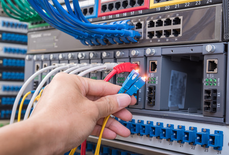 man working in network server room with fiber optic hub for digital communications and internet