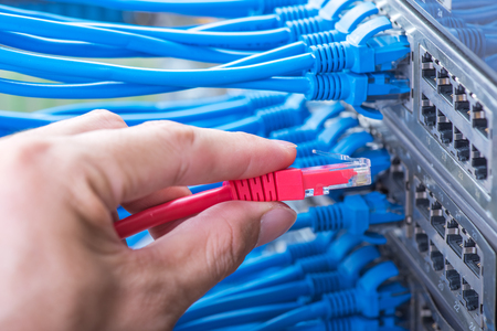 man working in network server room with fiber optic hub for digital communications and internet