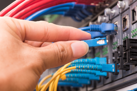 man working in network server room with fiber optic hub for digital communications and internetの写真素材