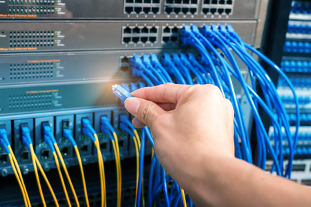 man working in network server room with fiber optic hub for digital communications and internet