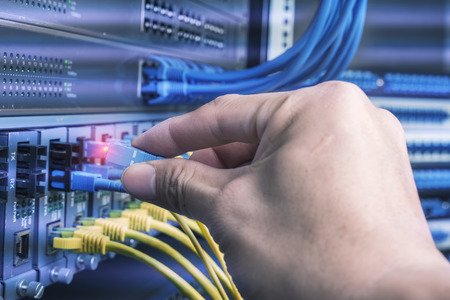 man working in network server room with fiber optic hub for digital communications and internet