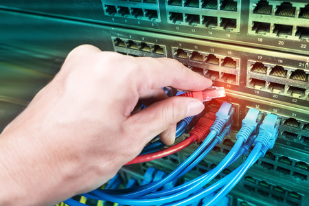 hand holding network cable on the switch hub in server room background