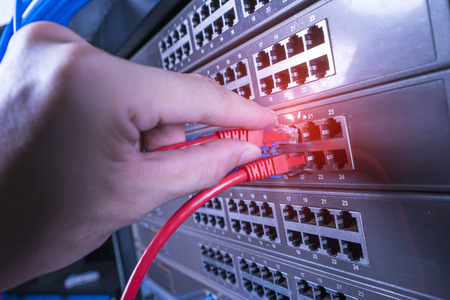 hand holding network cable on the switch hub in server room background
