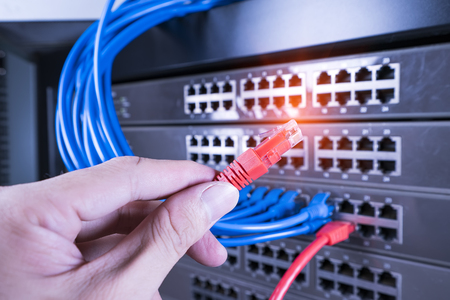 hand holding network cable on the switch hub in server room background