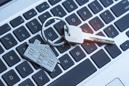 Key and keychain in the shape of a house on keyboard background.の写真素材