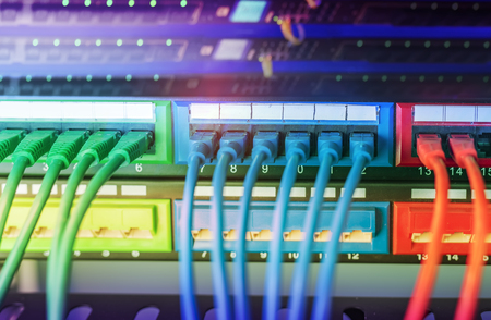 Server rack with blue and red internet patch cord cables connected to black patch panel in data...