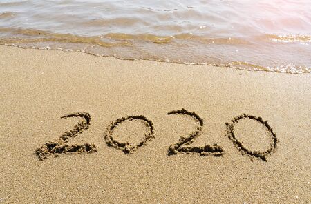 2020 year message handwritten in sand on beautiful beach background. New Years concept.