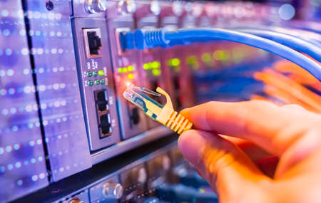 man working in network server room with fiber optic hub for digital communications and internet
