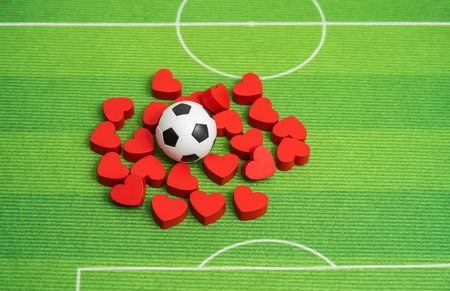 Football ball and red hearts on green grass background