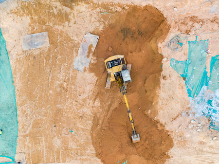 Excavator on earthmoving at construction site, aerial view.