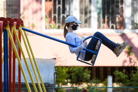 Girl in a protective mask swings on playground, amid coronavirus disease COVID-19 outbreak in Kyiv, Ukraine.のeditorial素材