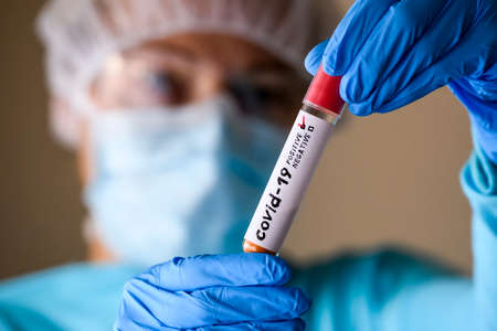 Woman in protective suit hold test tube with positive result infected with coronavirus COVID - 19....
