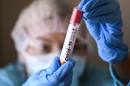 Woman in protective suit hold test tube with positive result infected with coronavirus COVID - 19....