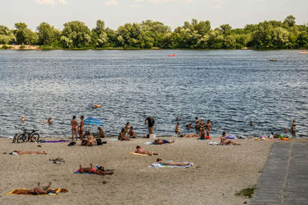 People sunbathe on the sandy beach near Obolon embankment in Obolon district in Kyiv, Ukraine. July 2020. High quality photoのeditorial素材