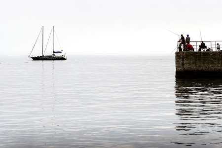 Silhouettes of fishermen on the pier on the background of the silhouette of a yacht on the calm sea. High quality photoの写真素材